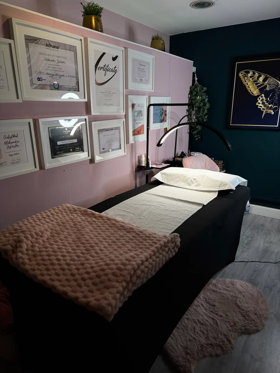 Lash Inspire studio with treatment bed, pink and teal walls, and framed certificates